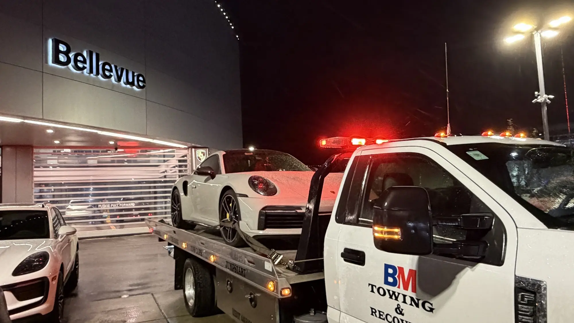 BM Towing flatbed transporting a Porsche 911 from a Bellevue dealership at night
